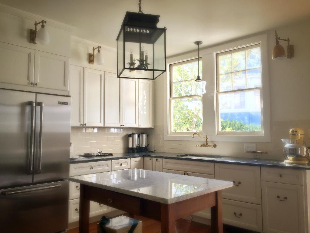 Bright white kitchen with a marble-topped island, lantern pendant and garden windows