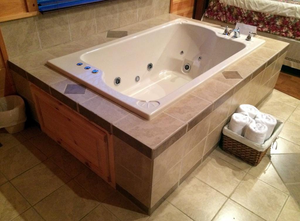 Jetted bathtub set into a tiled surround with rolled towels beside it