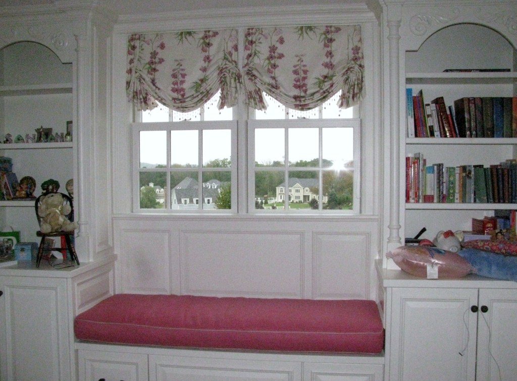 Window seat with a pink cushion between built-in white bookshelves